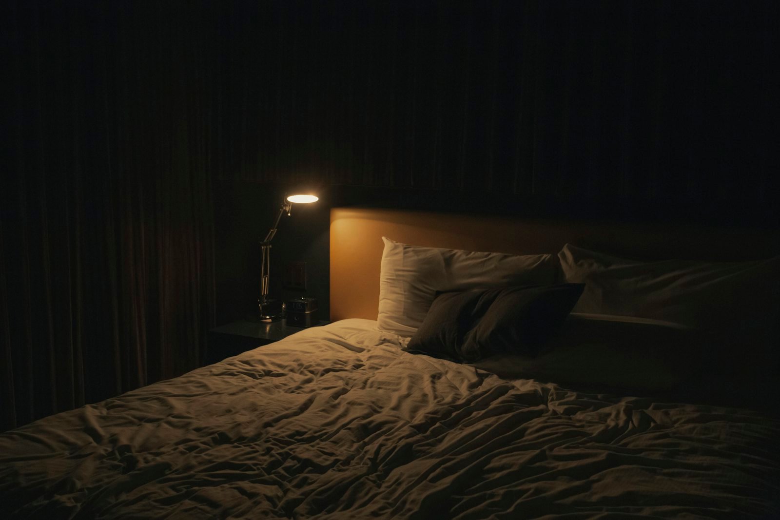 Bedroom at night lit by a single warm bedside lamp